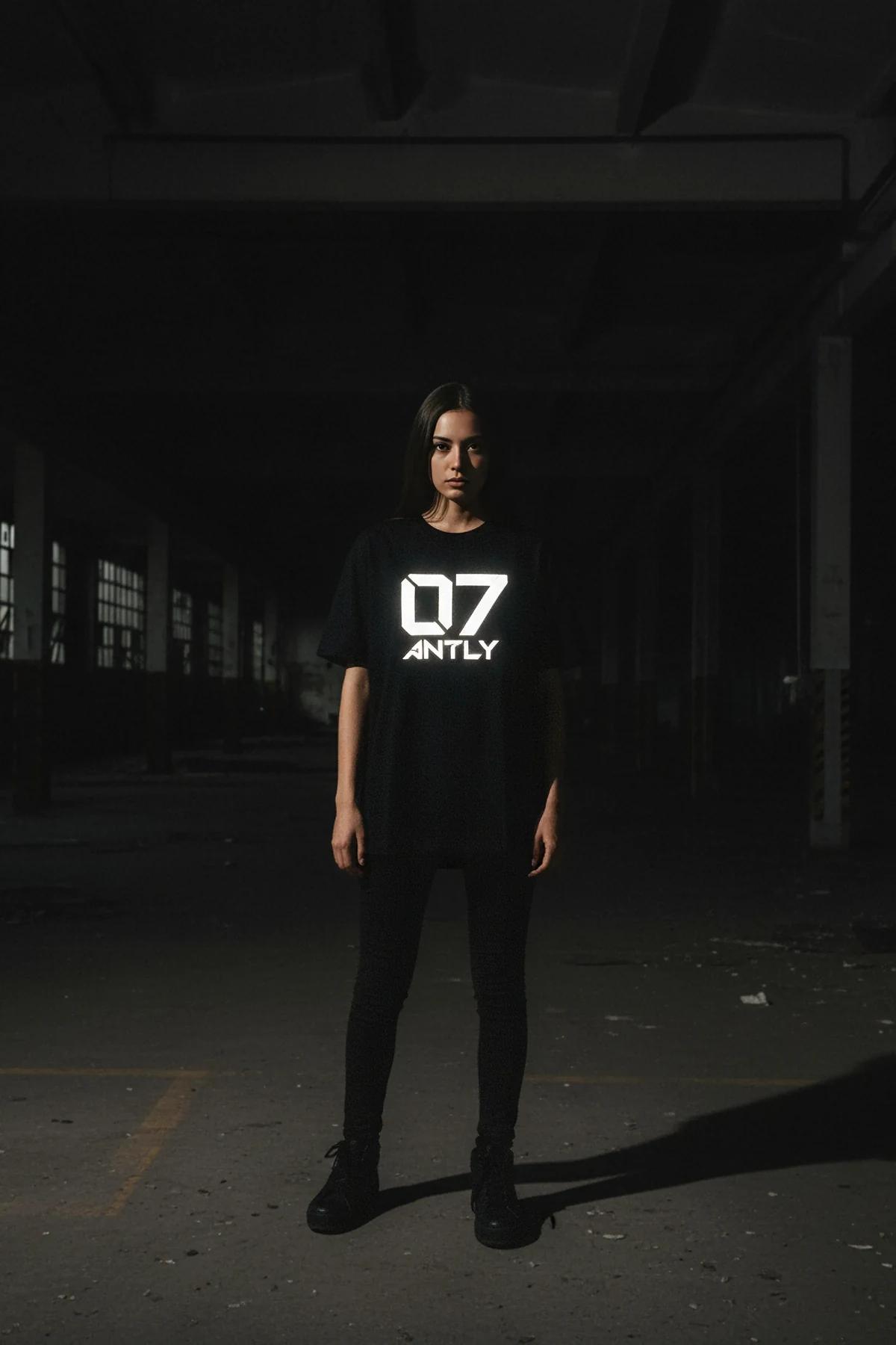 close-up of retroreflective ANTLY 07 white chest print on black cotton t-shirt under direct light