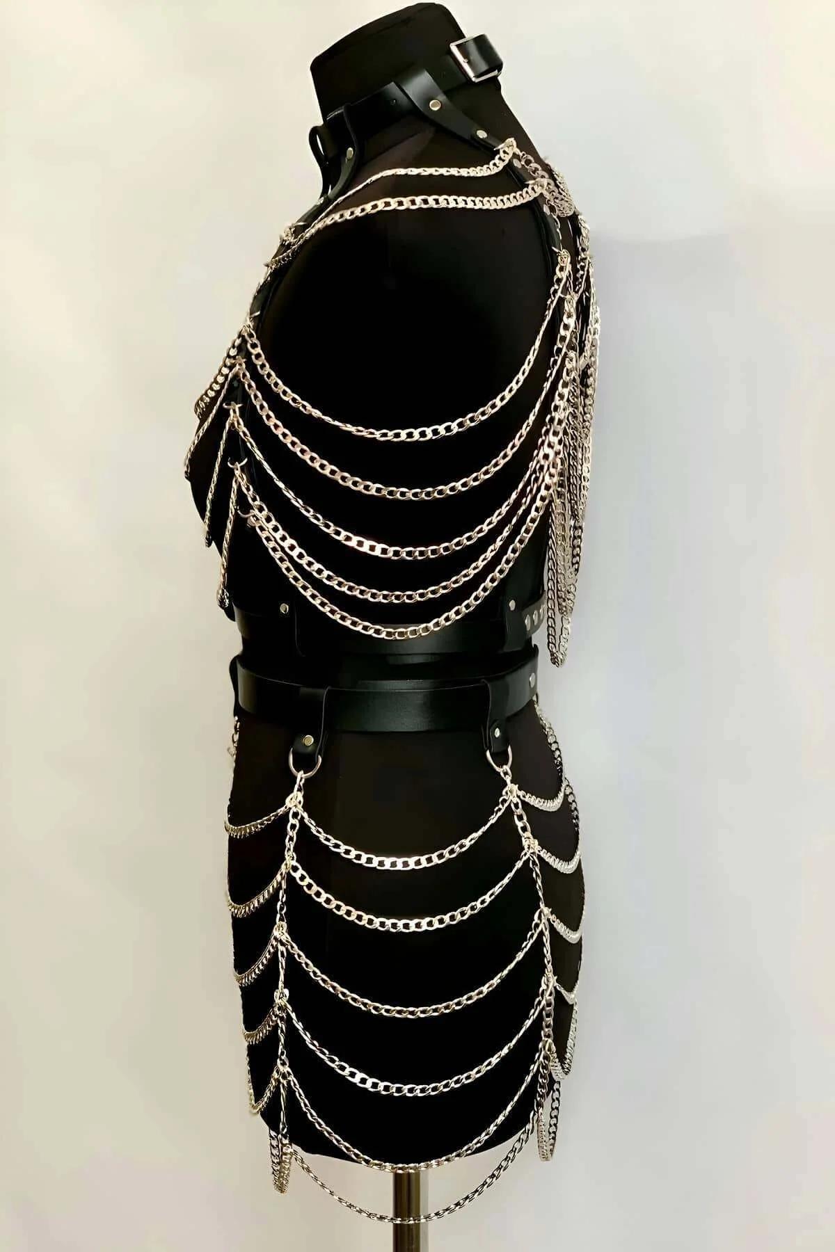 Full-length view of black faux leather harness set with silver chains worn over fishnet bodysuit