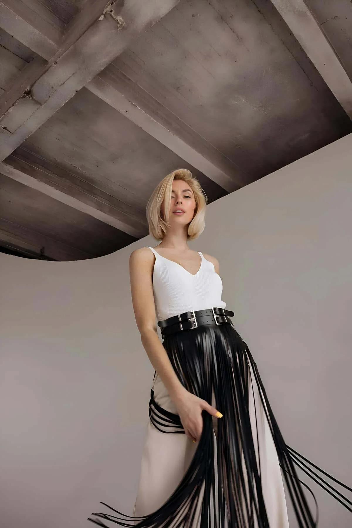 Front view of black fringe belt overlay layered over white trousers, full-length fringe silhouette