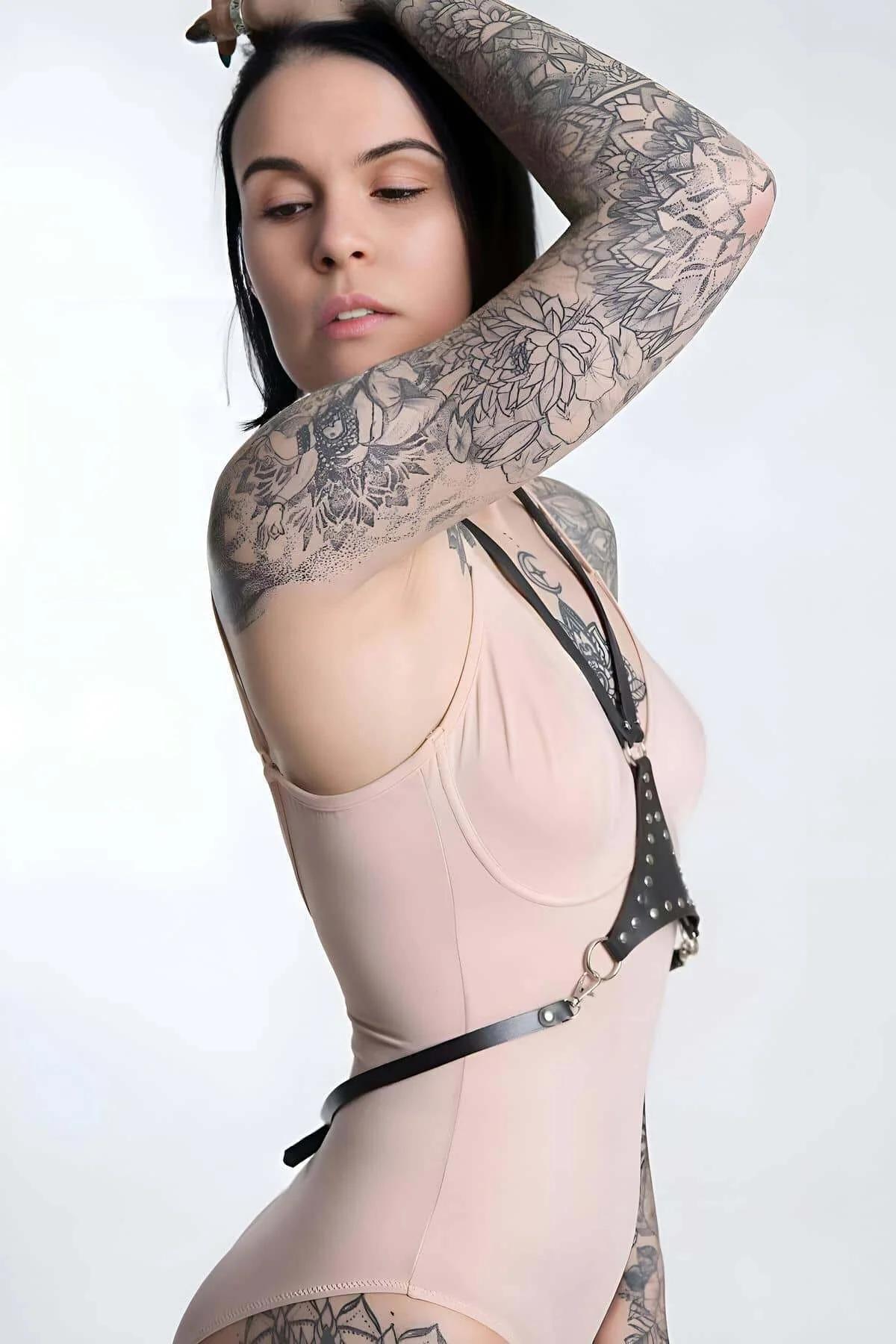 Adjustable black faux leather shoulder straps meeting at central silver O-ring on chest harness