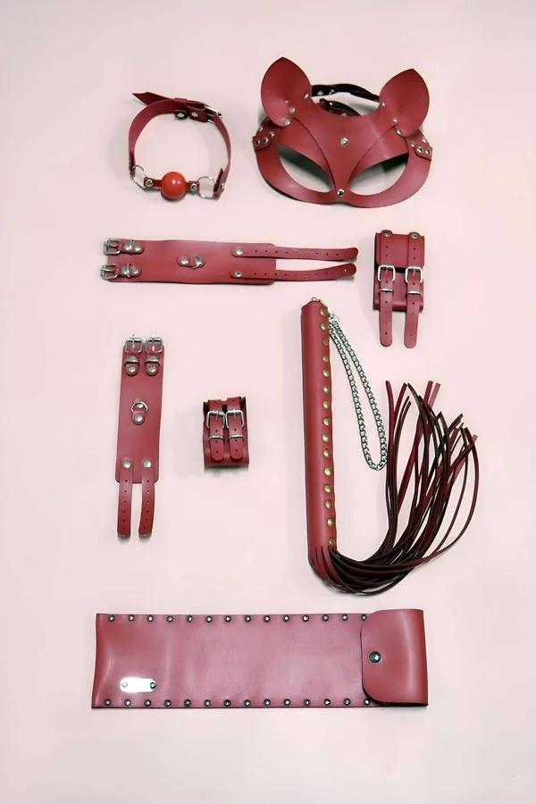 Red faux leather 7-piece accessory set with cat ear mask, double-buckle cuffs, studded flogger, collar, and riveted arm sleev