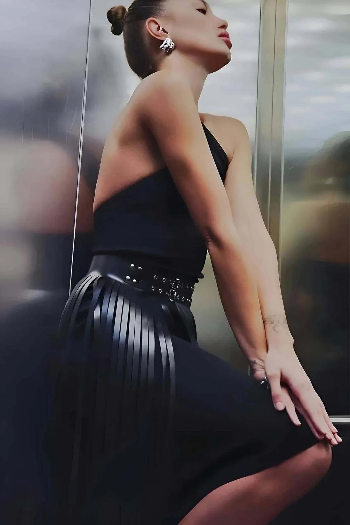 Full-length black faux leather tasseled skirt styled with pointed heels and halter top