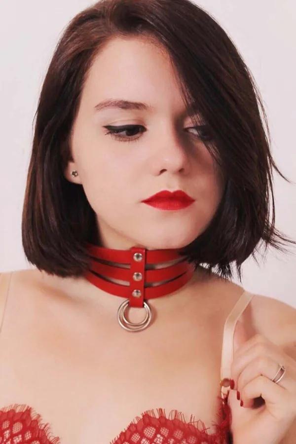 Triple strap red faux leather choker with silver rivets and central O-ring worn around the neck