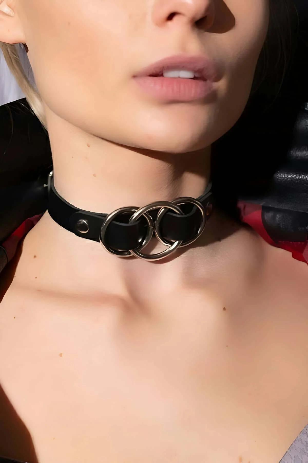Close-up of three polished silver O-rings threaded onto black faux leather choker band