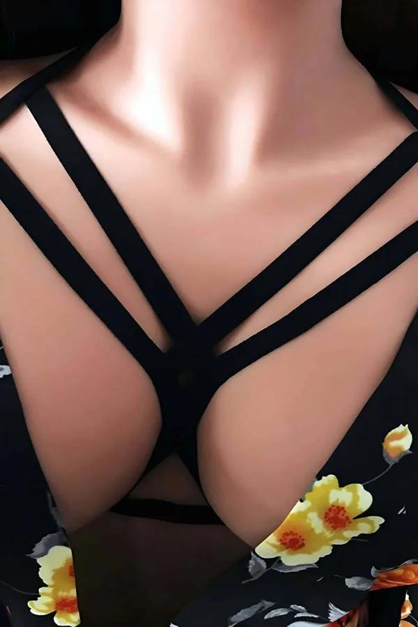 Strappy black vegan leather chest harness with criss-cross cage straps worn over floral dress, matte finish