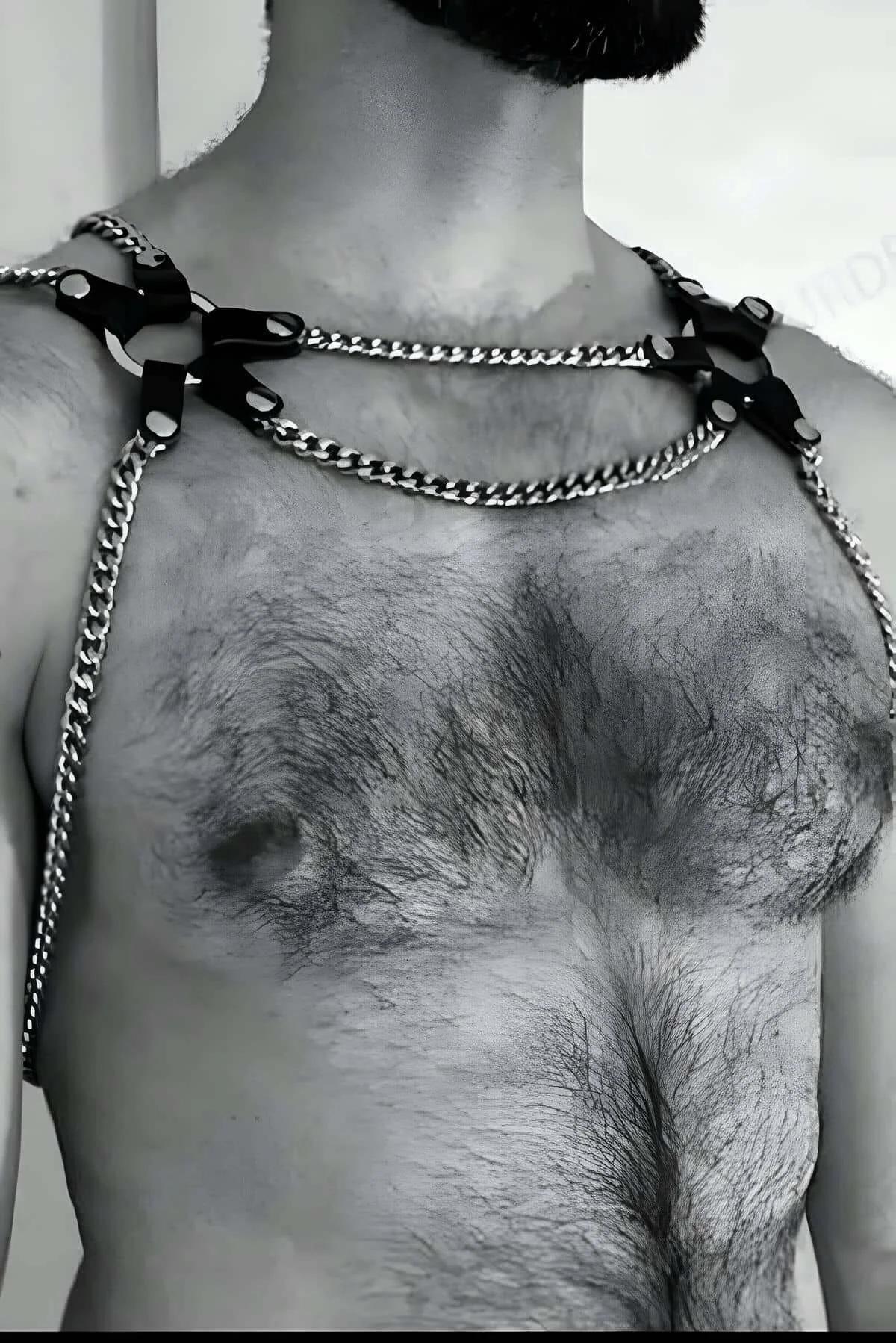 black faux leather shoulder harness with silver curb-link chains on male torso, adjustable strap tabs