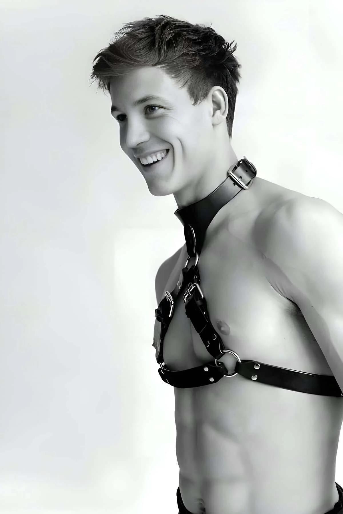 Close-up of silver pin buckle and D-ring hardware on black faux leather chest harness straps