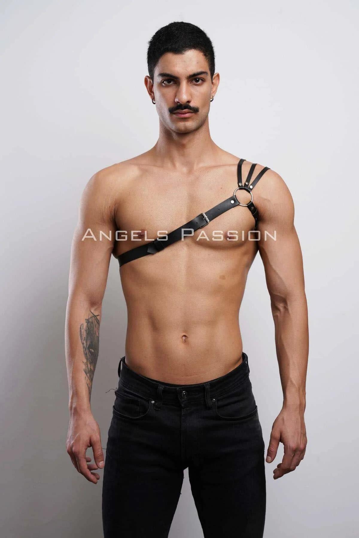 Black faux leather single strap chest harness with gold O-ring worn on male torso, diagonal strap from shoulder to waist