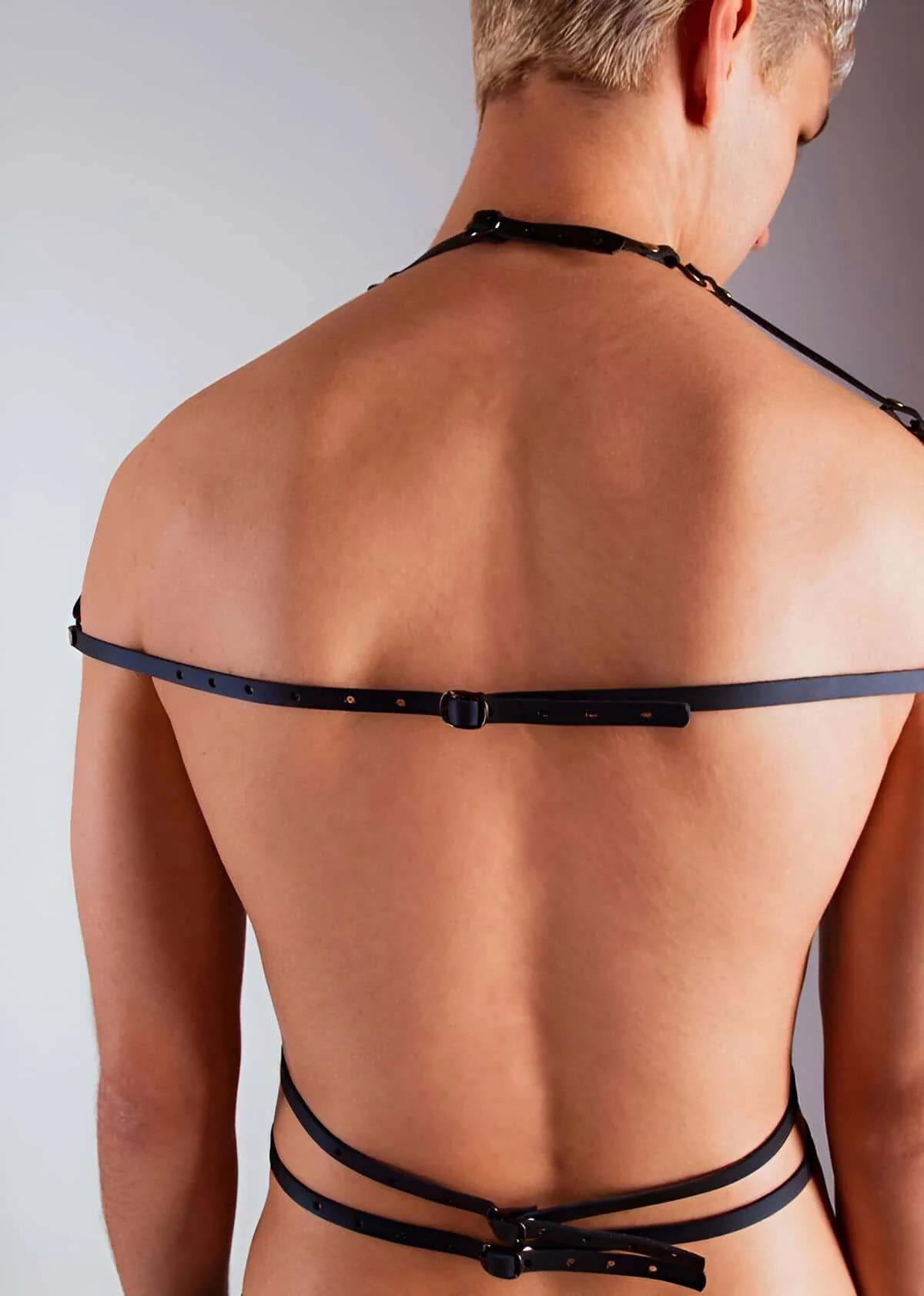 Close-up of antique brass dome rivets and O-ring detail on black faux leather chest harness strap crossing
