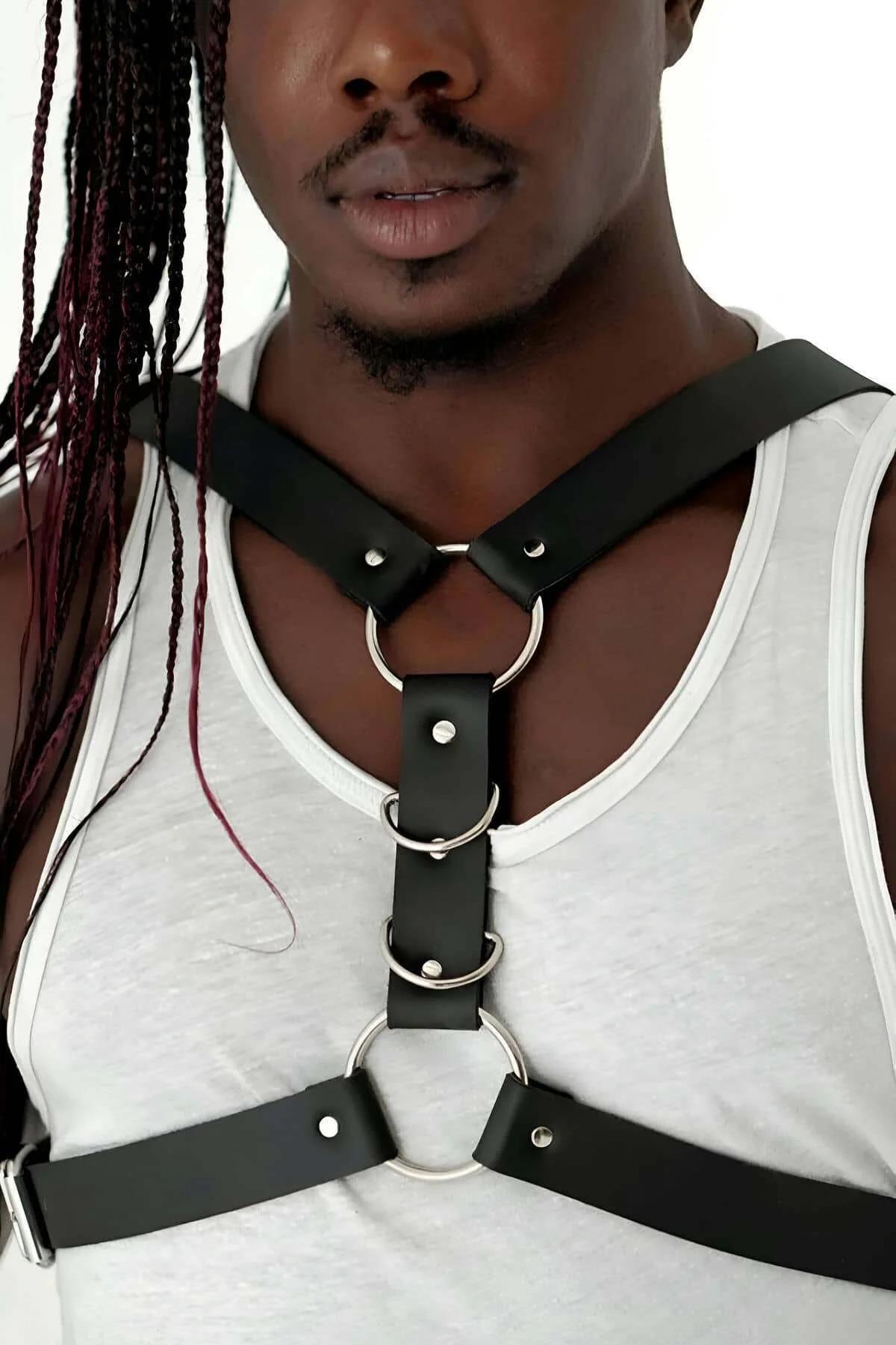 Front view of black PU leather chest harness showing triple gold O-ring vertical stack on bare chest
