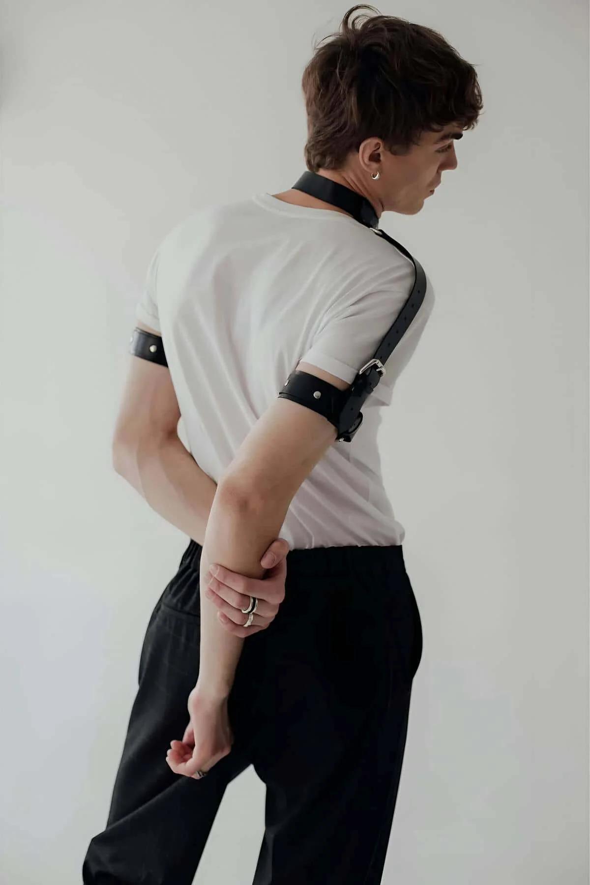 black faux leather bicep cuffs with silver buckle hardware on upper arms over white t-shirt