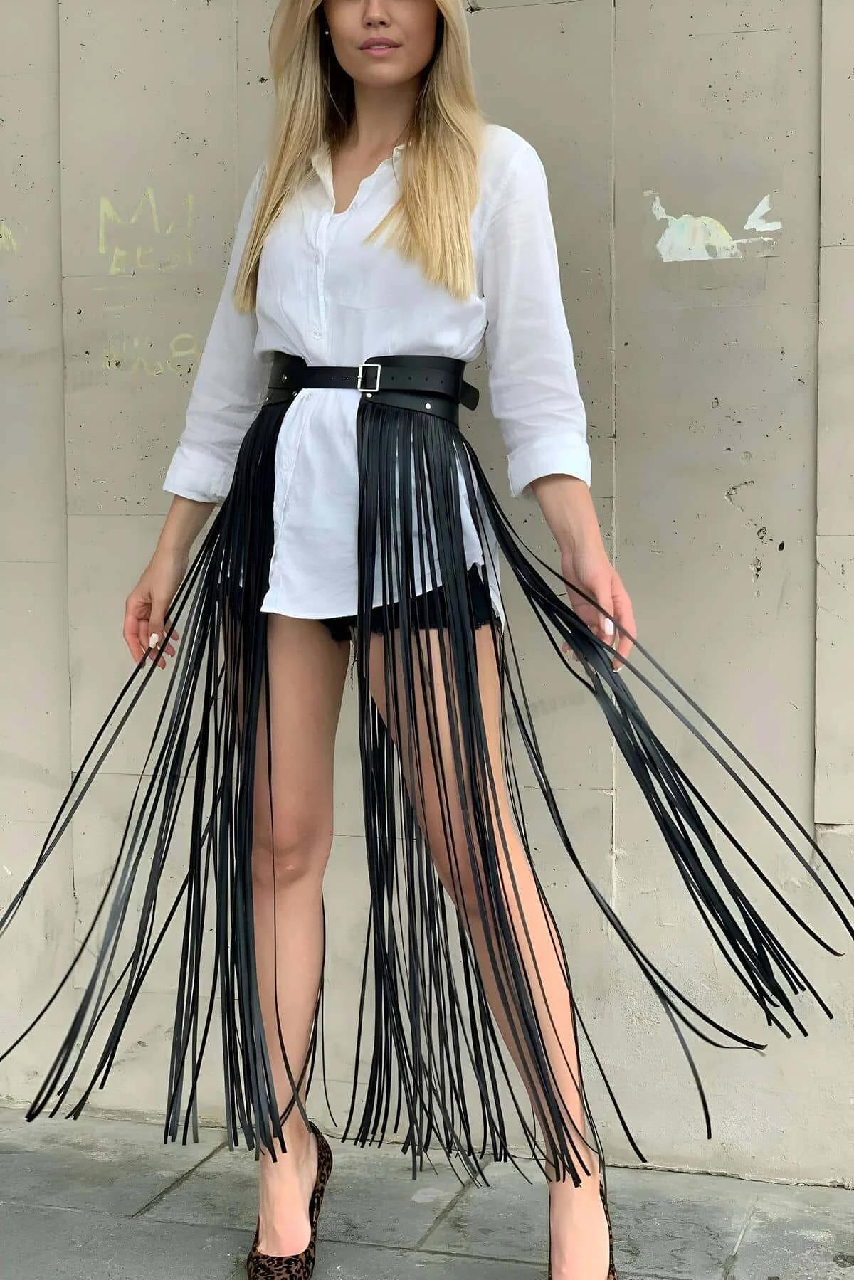 black faux leather fringe waist belt skirt with long tassels and adjustable buckle worn over white shirt and shorts