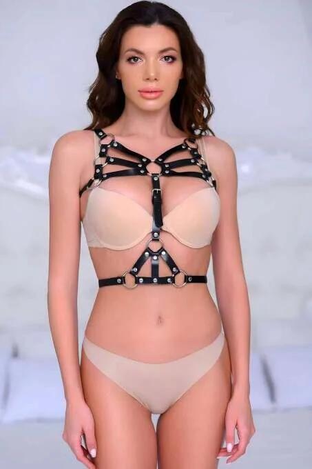 Black faux leather body harness with five silver O-rings and center buckle, worn over nude bralette
