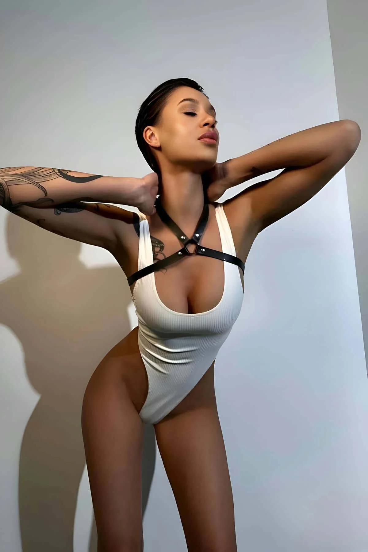 black faux leather halterneck chest harness with silver O-ring detail worn over white bodysuit