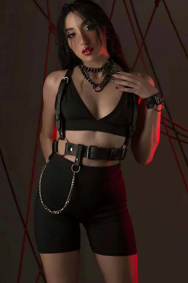 Black faux leather body harness with wide waist belt, silver O-rings, and detachable chain worn over black crop top