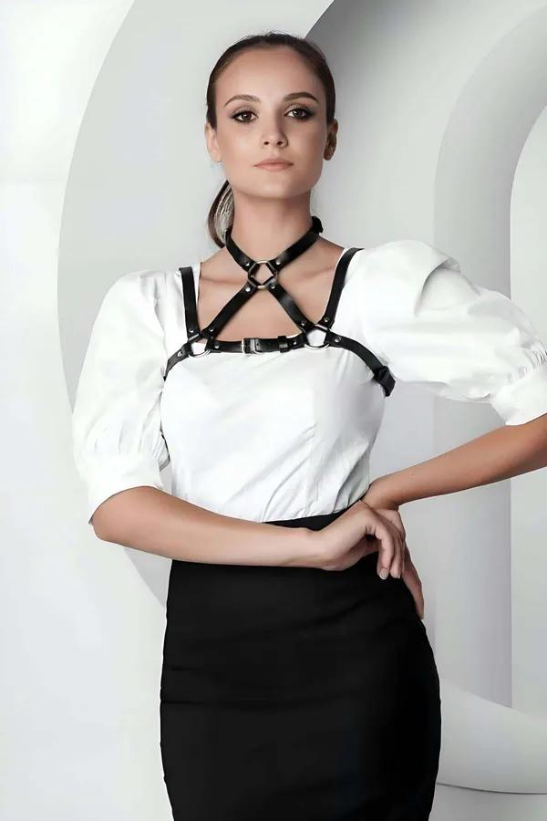 Black faux leather strappy O-ring chest harness with silver hardware worn over white blouse