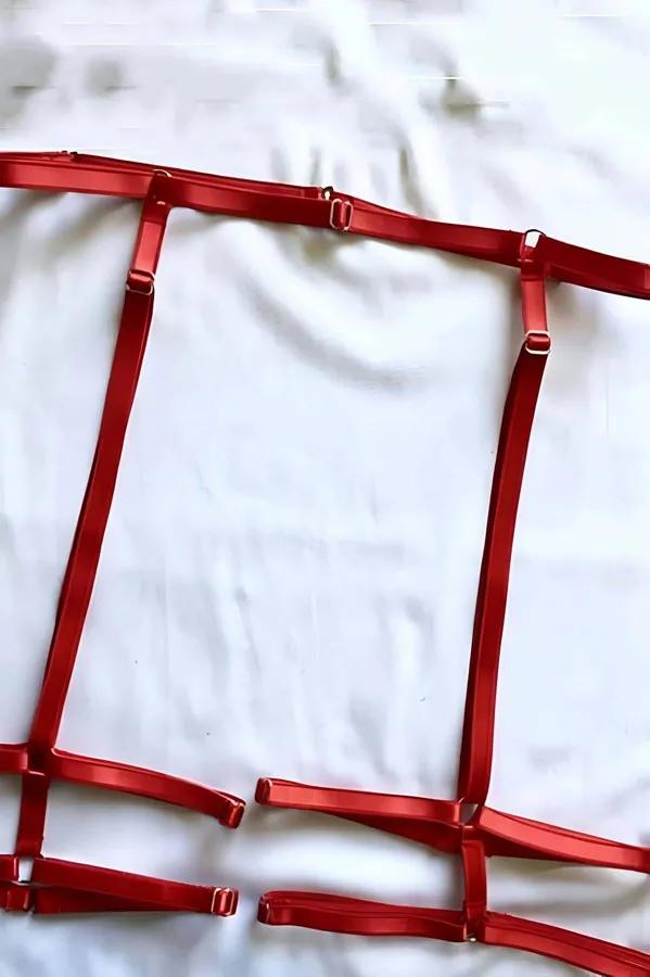Red strappy garter harness flat lay showing elastic grid strap construction with gold-tone slider hardware and adjustable thi