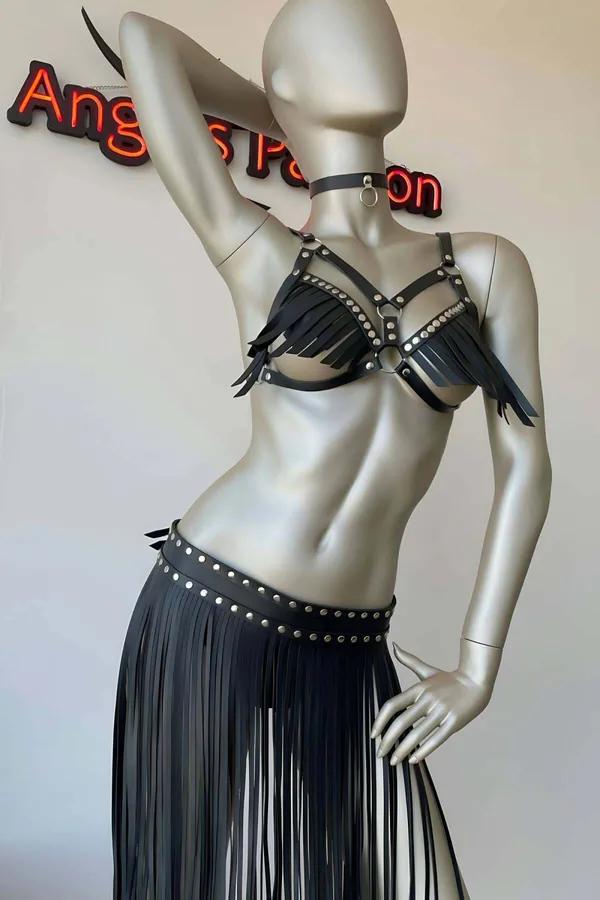 Black faux leather fringe harness bra with silver studs and O-ring, paired with matching studded waist fringe skirt on manneq