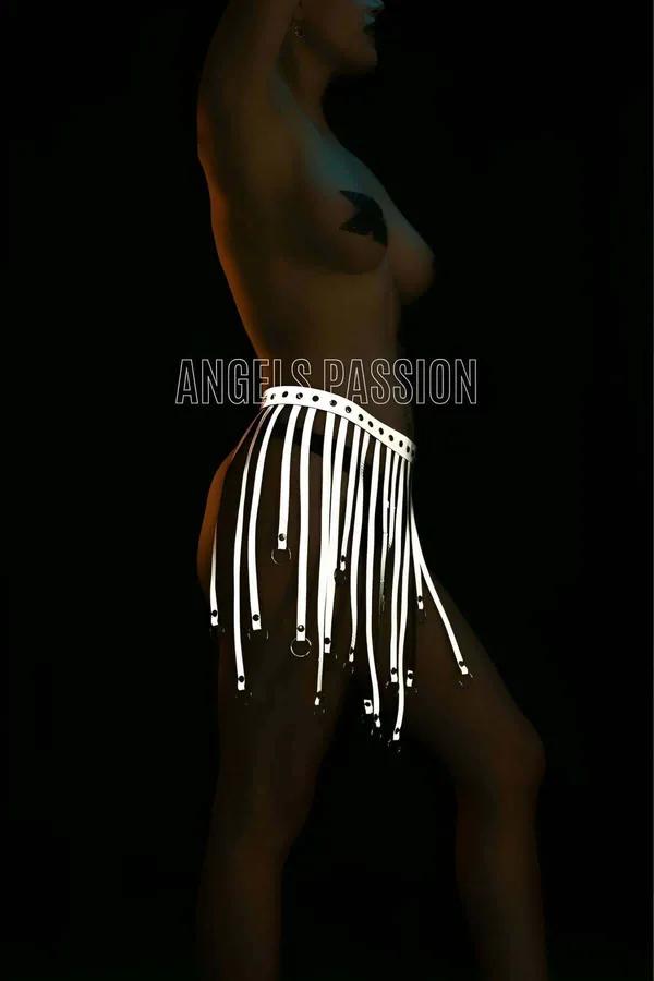 White reflective tassel body harness with silver O-ring tips worn at waist, fringe straps hanging to mid-thigh against dark b