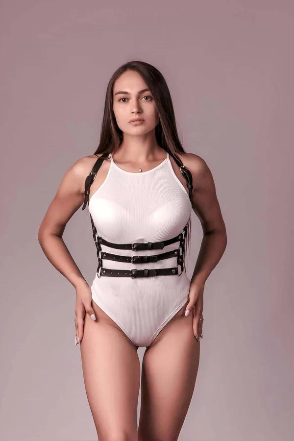 black faux leather 3-strap body harness with gold-tone buckles and D-rings worn over white ribbed bodysuit