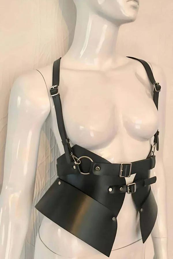 Black faux leather asymmetrical body harness with wide waist panel, shoulder straps, and silver buckle hardware on mannequin