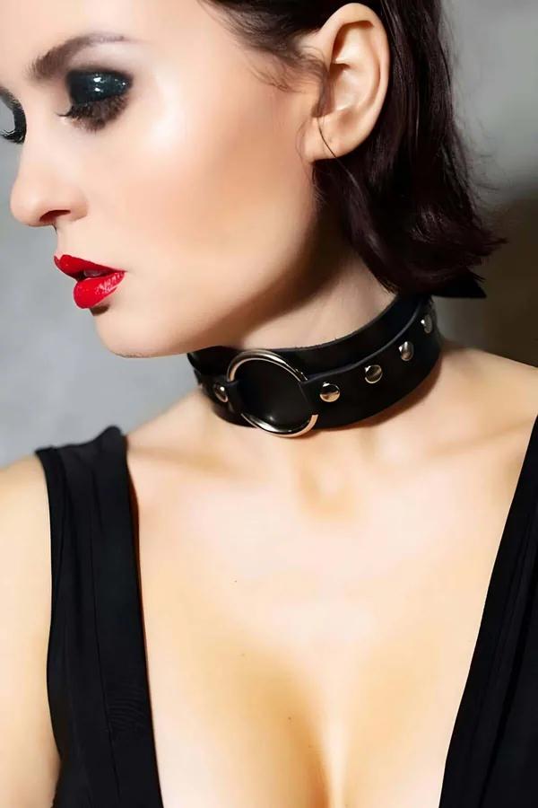 Wide black faux leather choker with silver O-ring and decorative studs worn around the neck, matte finish