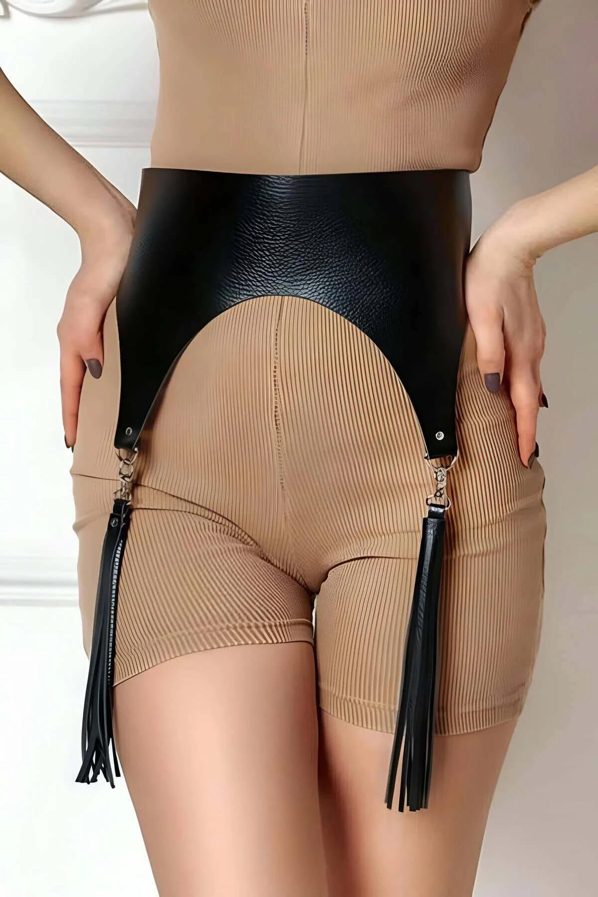 black faux leather wide waist harness with detachable tassels hanging at hips over beige ribbed shorts