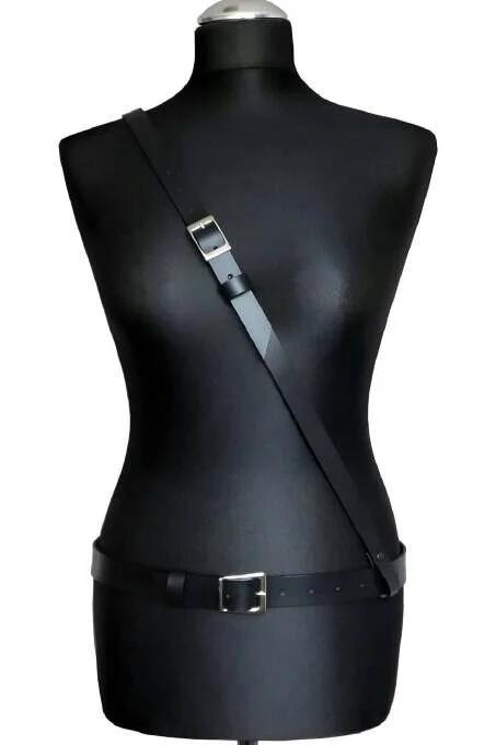 Minimalist black faux leather body harness with single diagonal shoulder strap and silver buckle waist belt on mannequin