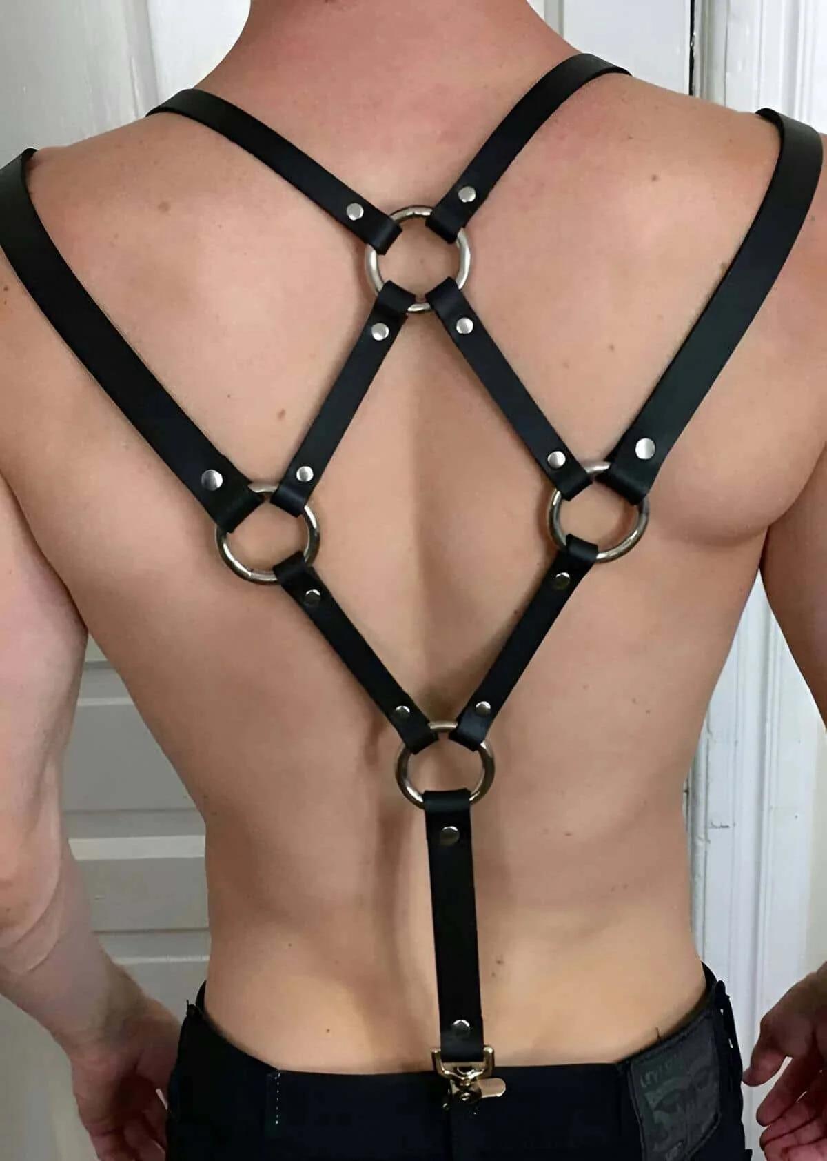 Black faux leather back harness with four silver O-rings and rivet hardware on male torso, rear view