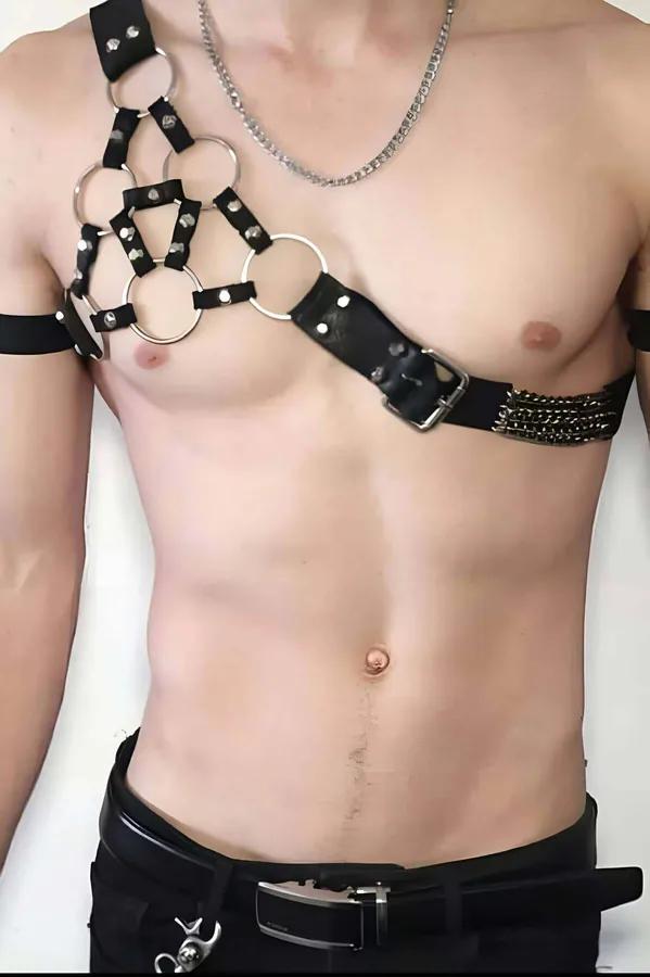 Black faux leather asymmetric chest harness with five silver O-rings on left shoulder and gold chain accent panel