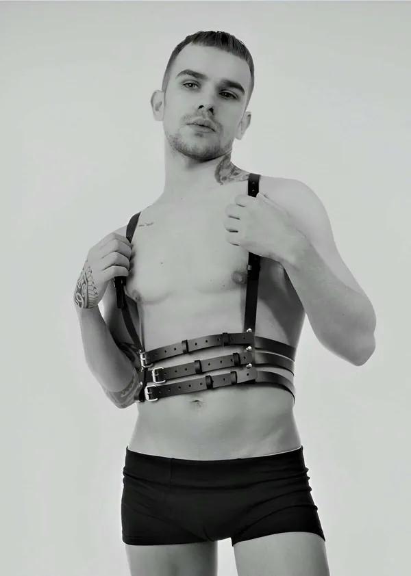black faux leather triple-strap chest harness with silver rectangular buckles worn by male model front view