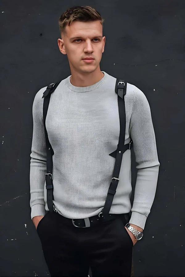 Black faux leather chest harness with silver buckles worn over grey knit sweater mens street style