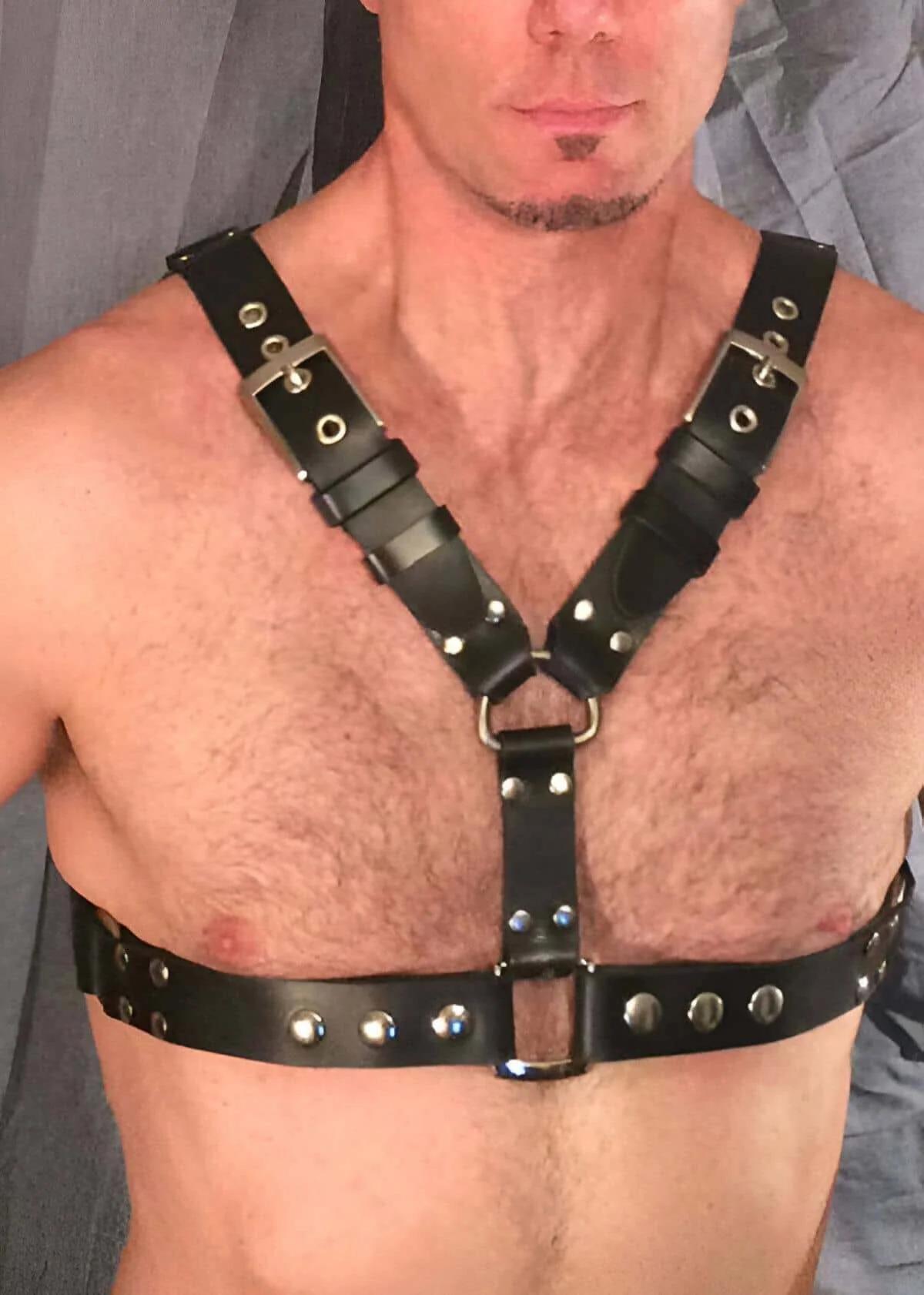 Black faux leather chest harness with silver buckles and dome rivets, Y-strap design with center D-ring, worn by a man