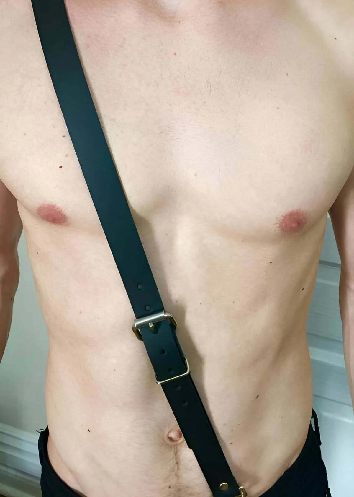 black faux leather single diagonal chest strap harness with gold-tone buckle on male torso