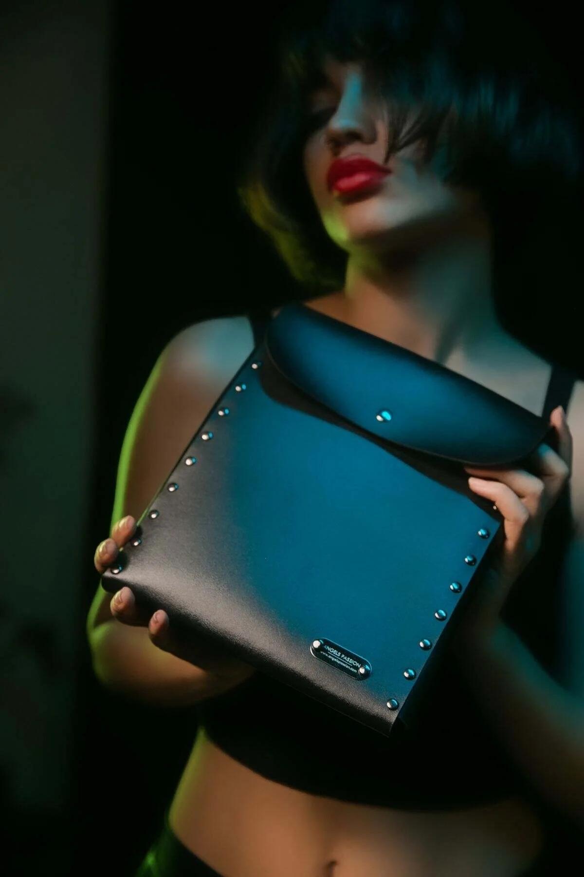 Black faux leather shoulder bag with silver edge studs and metal branding plate, structured rectangular shape