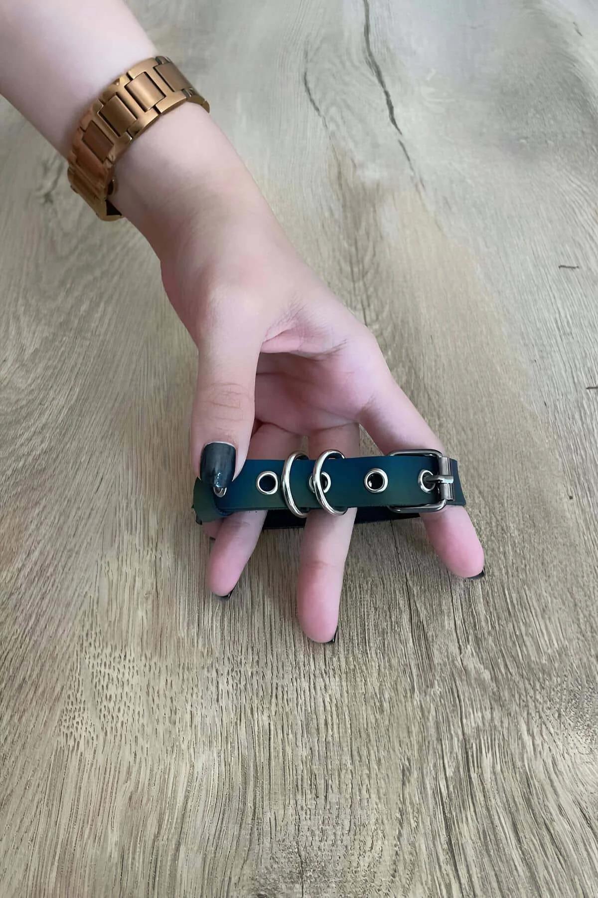 Iridescent teal faux leather finger harness with two silver O-rings and pin buckle worn across hand fingers