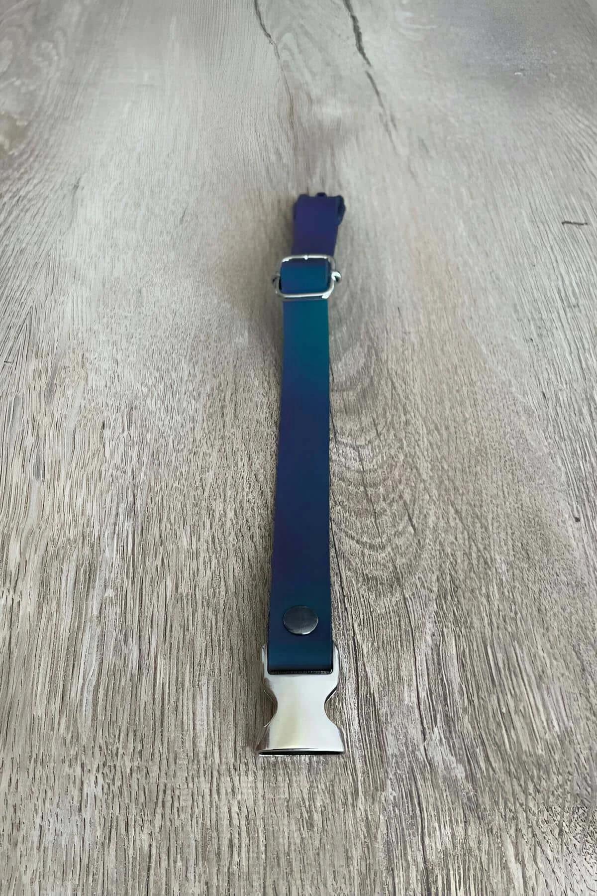 Blue reflective adjustable cat collar with silver metal quick-release buckle laid flat on wood surface