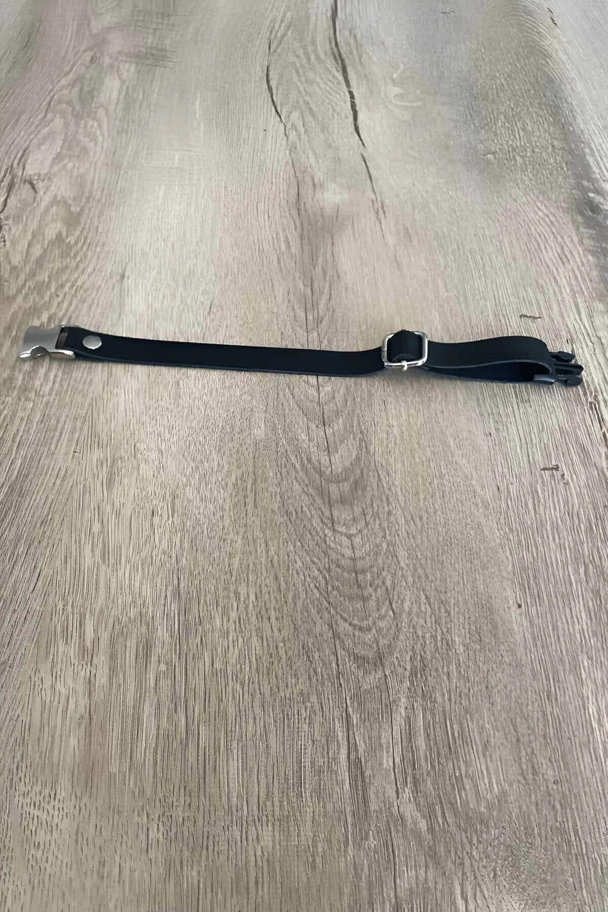 black faux leather collar with silver rectangular buckle and metal clip hardware laid flat on wood surface
